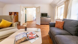 Una sala de estar acogedora con un sofá, una mesa de centro con revistas, un televisor y una estantería.
