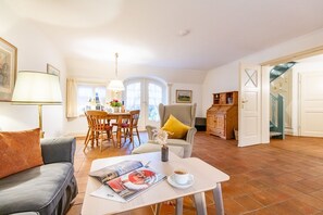 Un salon avec un canapé, une table basse sur laquelle se trouve un magazine, un coin repas avec une table et des chaises, et un escalier menant à l’étage supérieur.