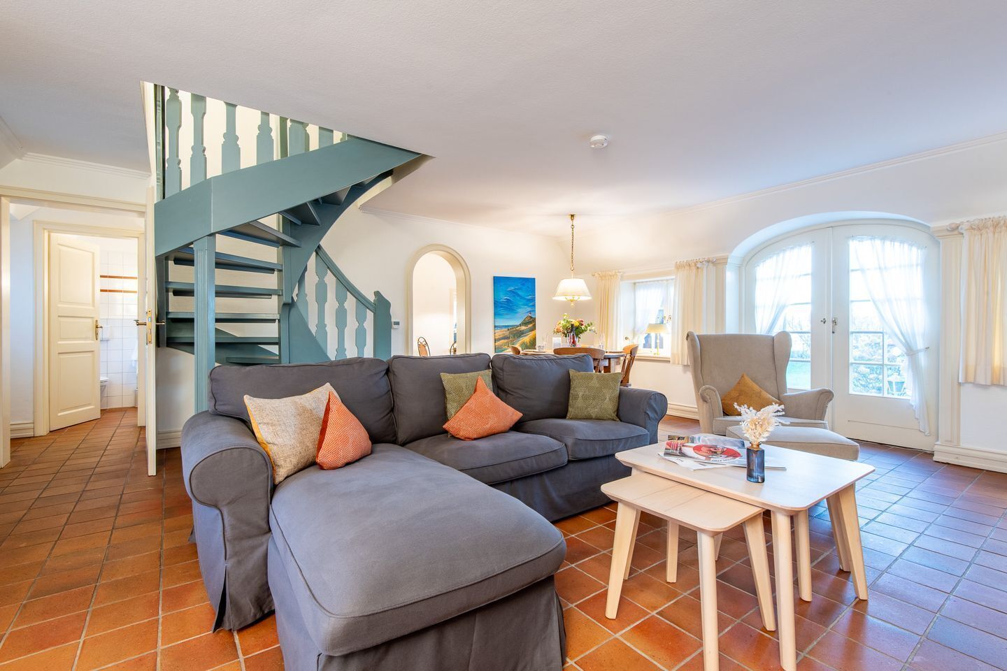 Ein Wohnzimmer mit einem grauen Ecksofa, einem Holztisch und einer blauen Wendeltreppe.