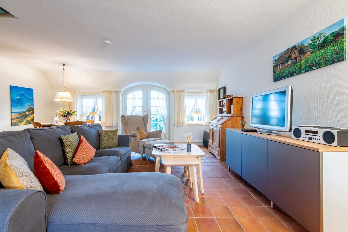Ein modernes Wohnzimmer mit grauem Sofa, einem Esstisch und einer Küchenzeile mit Fernseher und Radio.