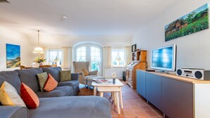 Un soggiorno moderno con un divano grigio, un tavolo da pranzo e un angolo cucina con TV e radio.