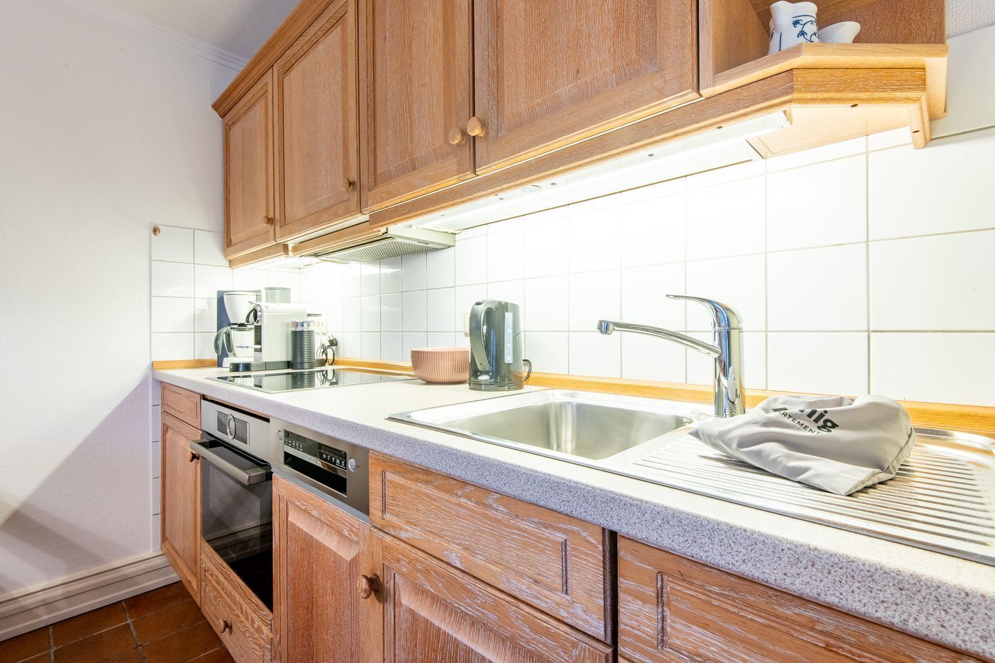 A kitchen with wooden cabinets, a stainless steel sink, a coffee maker, and a dish drying rack.