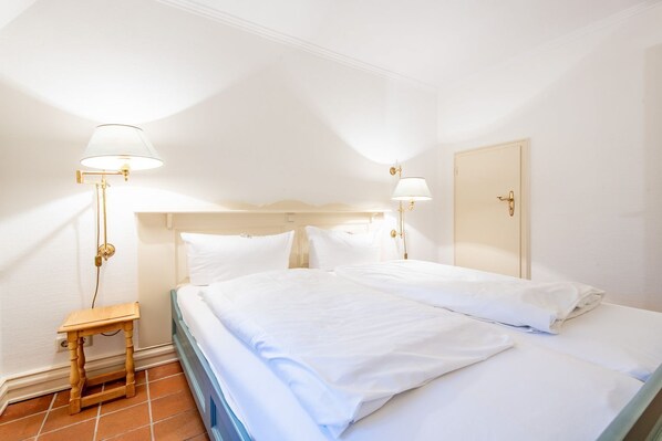 A hotel room with a large bed, two bedside lamps, a wooden nightstand, and a door.