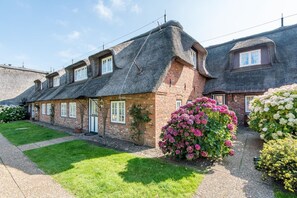 A traditional brick house with a thatched roof, a well-maintained garden, and a gravel driveway.