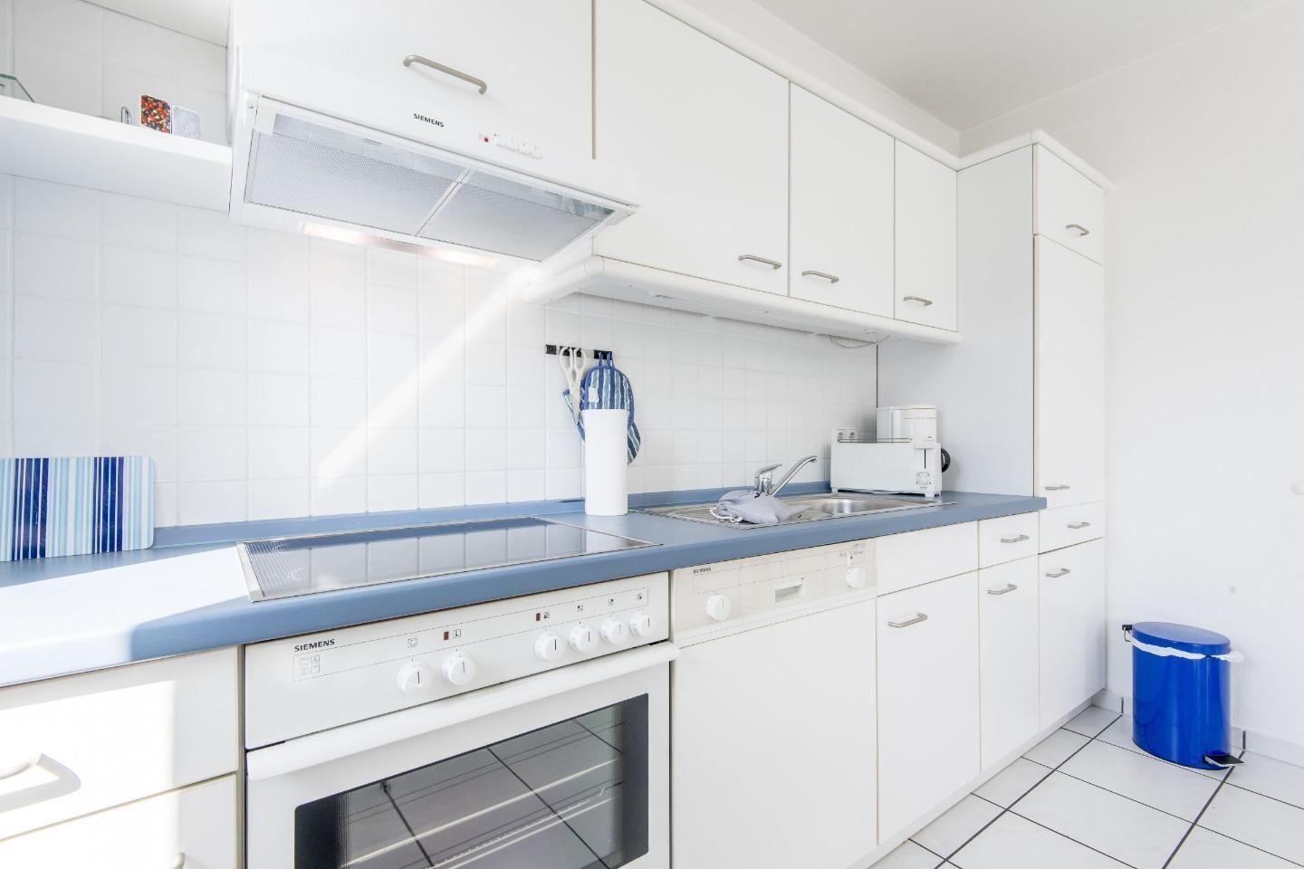 Une cuisine moderne avec des meubles blancs, un plan de travail bleu, une cuisinière Siemens et une machine à café.