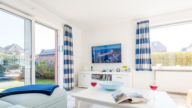 En moderne stue med sofa, sofabord med skål og vinglas, fjernsyn og reol.