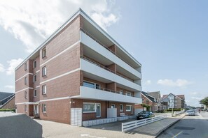Ein mehrgeschossiges Wohngebäude mit Backsteinfassade, Balkonen und einem Parkplatz.