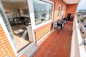 Ein Balkon mit Fliesenboden, eine Sitzecke mit Stühlen und Tisch, und Blick auf die Stadt durch große Fenster.