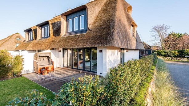 A house with a thatched roof, large windows, and a wooden deck.