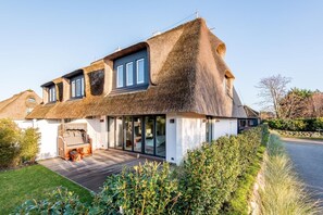 Una casa con techo de paja, ventanas grandes y una terraza de madera.