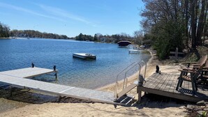 A wooden dock extending into a lake with clear water, surrounded by a sandy beach and a few chairs. - Silver Lake Waterfront Home, Traverse City, MI (Traverse City)