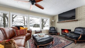 A living room with leather sofas, a fireplace, and large windows. - Silver Lake Waterfront Home, Traverse City, MI (Traverse City)