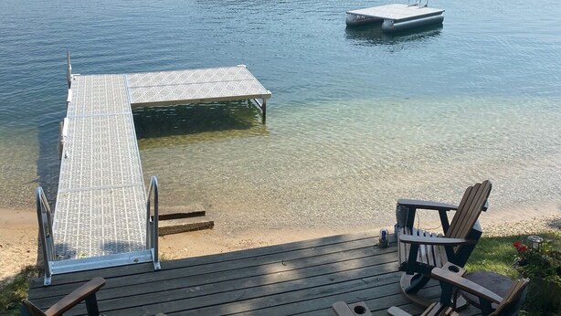A wooden deck with Adirondack chairs overlooking a lake, a dock, and a small boat. - Silver Lake Waterfront Home, Traverse City, MI (Traverse City)
