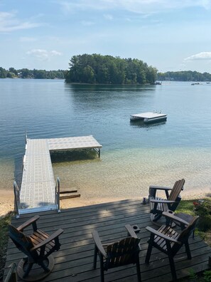 A wooden deck with Adirondack chairs overlooking a lake, a dock, and a small boat. - Silver Lake Waterfront Home, Traverse City, MI (Traverse City)