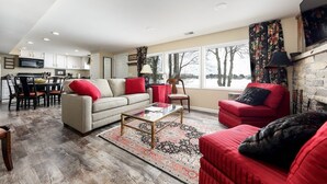 A spacious living room with a sofa, armchairs, and a coffee table. There is a dining area with a table and chairs, and a kitchen in the background. - Silver Lake Waterfront Home, Traverse City, MI (Traverse City)