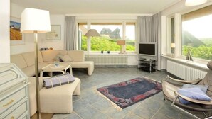 Habitación bien iluminada con sofá, sillón, televisor y vistas al exterior.