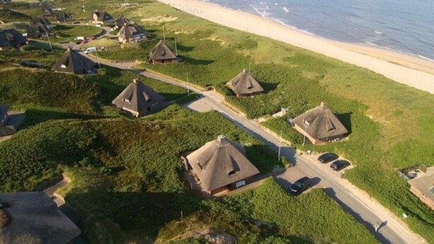Vista aérea de una zona costera con cabañas de techo de paja, una playa y una carretera.
