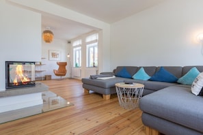 Un salon moderne avec une cheminée, un canapé gris agrémenté de coussins bleus, une table basse ronde et un plancher en bois.