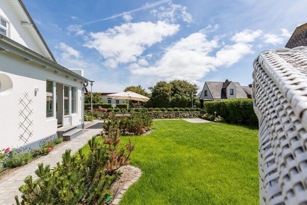 Un jardin bien entretenu, avec un chemin pavé, une pelouse et un bâtiment blanc doté d’une fenêtre et d’une porte.