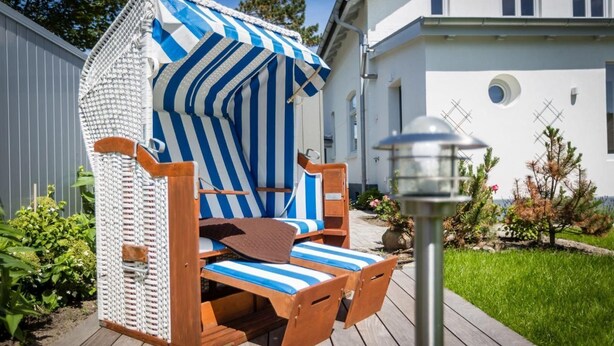 Une chaise de plage dotée d’un parasol à rayures et d’une structure en bois, placée sur une terrasse en bois.