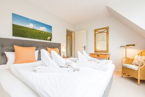 A hotel room with a large bed, a painting of a green field, a mirror, a wicker chair, and a nightstand with a lamp. - Ostertresker 54, island oasis (Sylt-Ost)