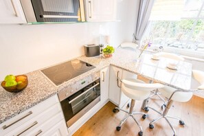 Une cuisine moderne dotée d’une cuisinière et d’un four intégrés, ainsi que d’un coin repas avec une table en verre et des chaises blanches.
