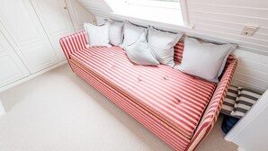Ein rot-weiß gestreiftes Schlafsofa mit Kissen, ein Fenster und eine weiße Tür in einem Raum mit weißen Wänden und Teppich.
