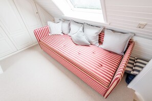 A red and white striped sofa bed with pillows, a window, and a white door in a room with white walls and carpet.