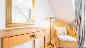 Ein Zimmer mit einem Holzkasten, einem Korbstuhl, einer Stehlampe und einem großen Spiegel.