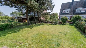 Ein gepflegter Rasen mit Holzzaun, einer kleinen Gartenhütte und einem Haus mit Ziegeldach im Hintergrund.