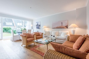 Un salon moderne avec une table basse en verre, des fauteuils en osier et un canapé blanc.