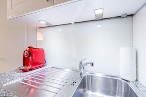 Une cuisine moderne équipée d’un évier en acier inoxydable, d’une machine à café rouge et d’un distributeur d’essuie-tout.