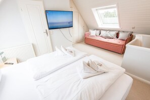 A hotel room with a bed, a TV mounted on the wall, a window, and a built-in bench with pillows. - Ostertresker 54, island oasis (Sylt-Ost)