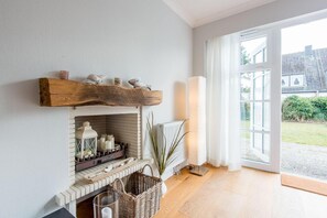 A cozy room with a fireplace, a large window, and a view of the outside. - Ostertresker 54, island oasis (Sylt-Ost)