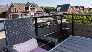 A balcony with a wicker chair and a table, overlooking a residential area with houses and parked cars. - House Doktor-Ross-Straße 25, Whg. 19 Wunderkammer (Sylt)