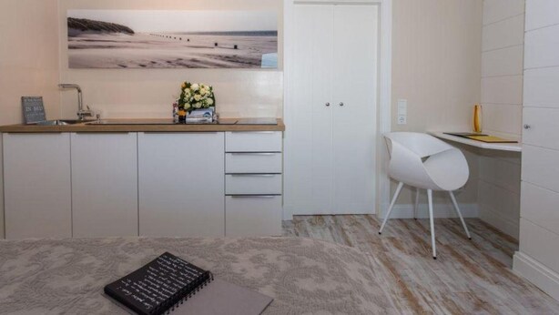 A small, modern room with a bed, a desk, a chair, a white door, and a large beach photograph on the wall. - House Doktor-Ross-Straße 25, Whg. 19 Wunderkammer (Sylt)