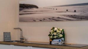 A kitchen with a wooden countertop, a sink, a flower arrangement, and a wall-mounted picture of a beach. - House Doktor-Ross-Straße 25, Whg. 19 Wunderkammer (Sylt)