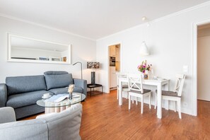 A modern living room with a grey sofa, a glass coffee table, and a dining area with white chairs and a table. - Haus Dünenburg, Whg. 24 - Gemütlich. Zentral. Strandnah. - Objekt-id: Hdb/24 (Sylt)
