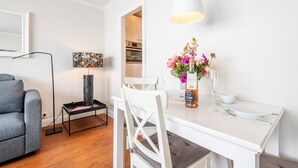 A dining area with a white table, chairs, a vase of flowers, a bottle of champagne, and a modern lamp. - Haus Dünenburg, Whg. 24 - Gemütlich. Zentral. Strandnah. - Objekt-id: Hdb/24 (Sylt)