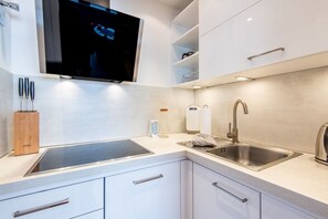 A modern kitchen with a built-in stove, a sink, and a flat-screen TV mounted above the counter. - Haus Dünenburg, Whg. 24 - Gemütlich. Zentral. Strandnah. - Objekt-id: Hdb/24 (Sylt)