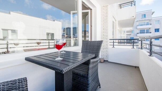 A balcony with a table and chairs, two glasses of red wine, and a view of buildings. - Haus Dünenburg, Whg. 24 - Gemütlich. Zentral. Strandnah. - Objekt-id: Hdb/24 (Sylt)