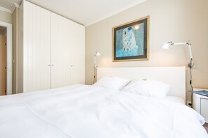 A neatly made bed with white linens, a framed artwork above it, and a bedside lamp on the right. - Haus Dünenburg, Whg. 24 - Gemütlich. Zentral. Strandnah. - Objekt-id: Hdb/24 (Sylt)