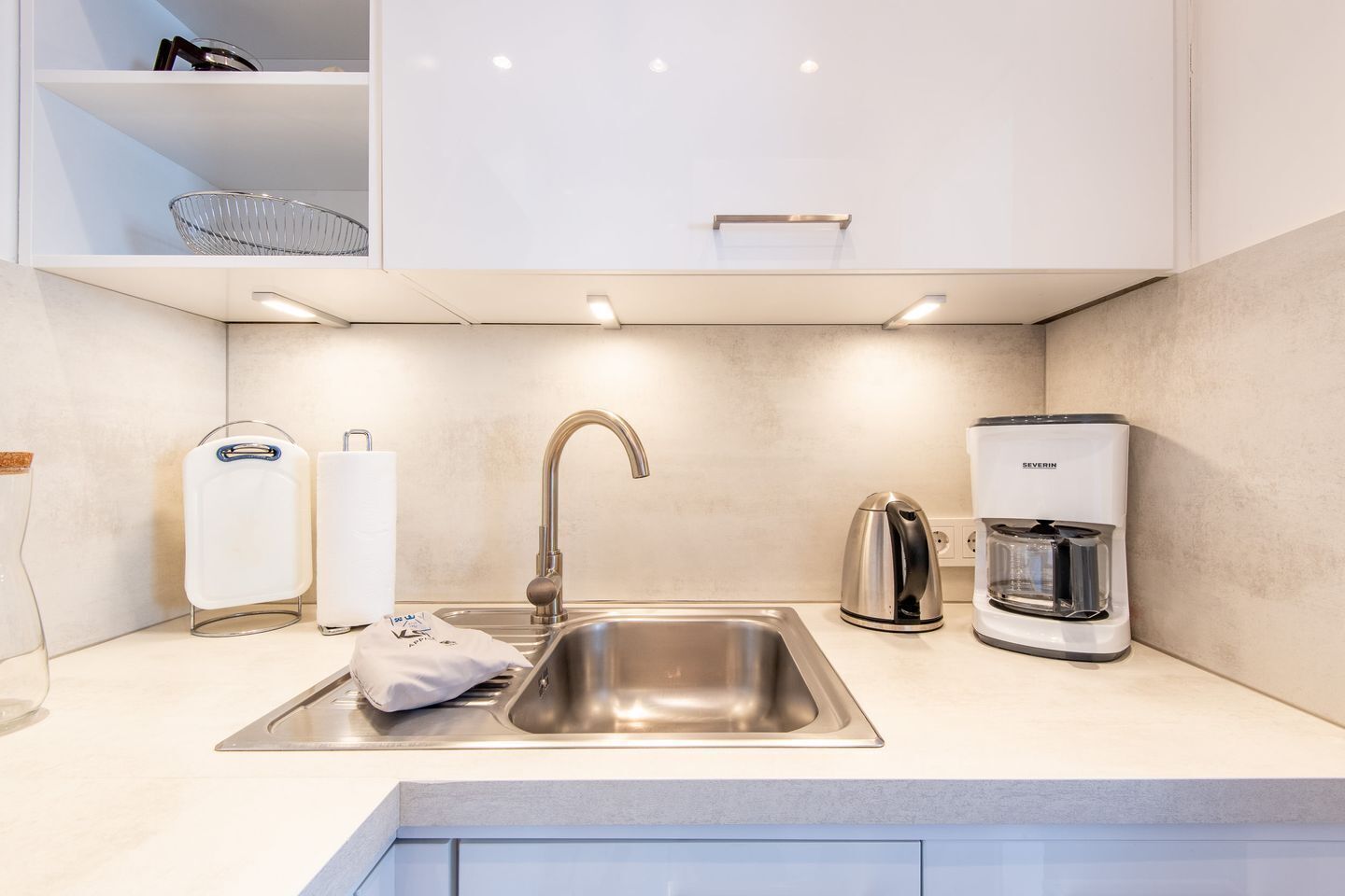 A modern kitchen with a stainless steel sink, a kettle, and a coffee maker.