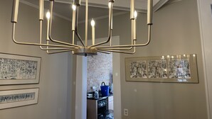 Un lustre doté de plusieurs points lumineux, dans une pièce dont les murs sont ornés d’œuvres d’art encadrées.