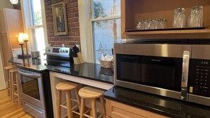 Une cuisine avec des meubles en bois, un four à micro-ondes en acier inoxydable, un four et un tabouret de bar.
