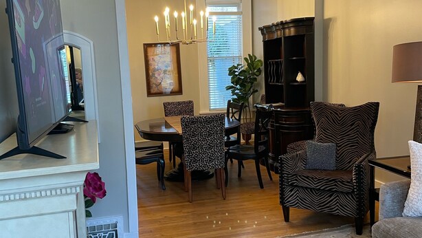 Un salon avec une cheminée, un coin repas et une cuisine visible à travers une porte ouverte.