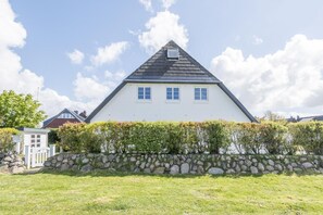A white house with a steeply pitched roof, a small dormer window, and a stone wall in the foreground.