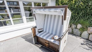 A wooden outdoor seating area with a striped cushion and a small table with a cup. - Country house Tinnumburg, Germany (Sylt-Ost)