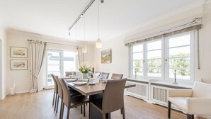 A dining room with a long table set for six, large windows with curtains, and a white radiator below. - Country house Tinnumburg, Germany (Sylt-Ost)
