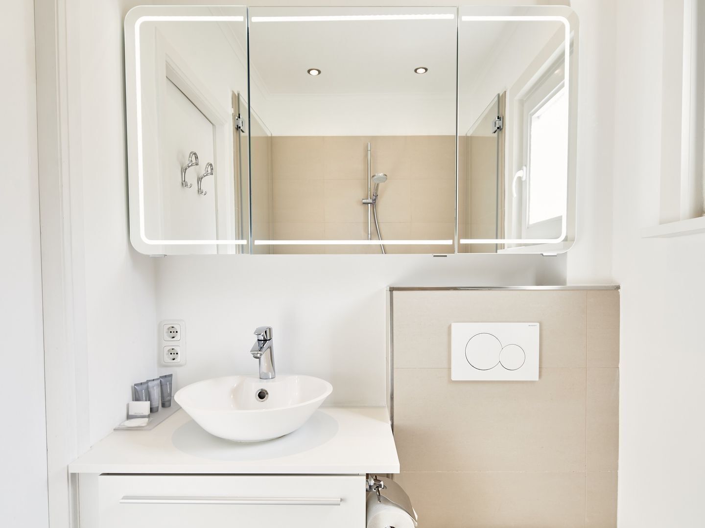 A modern bathroom with a white sink, a mirror with integrated lighting, and a shower area.